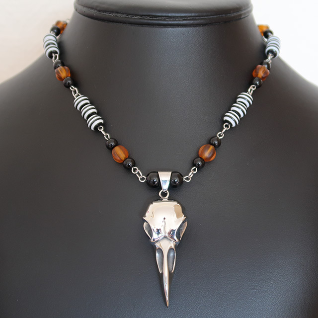 A stainless steel necklace with a raven or bird skull centrepiece, and orange glass pumpkin beads